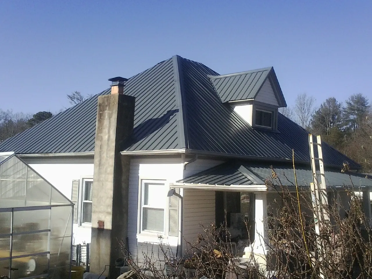 Dark blue standing seam metal roof on a white farmhouse with dormer — Slate & Tile Roof Repair by Roofing Brothers in Plaistow