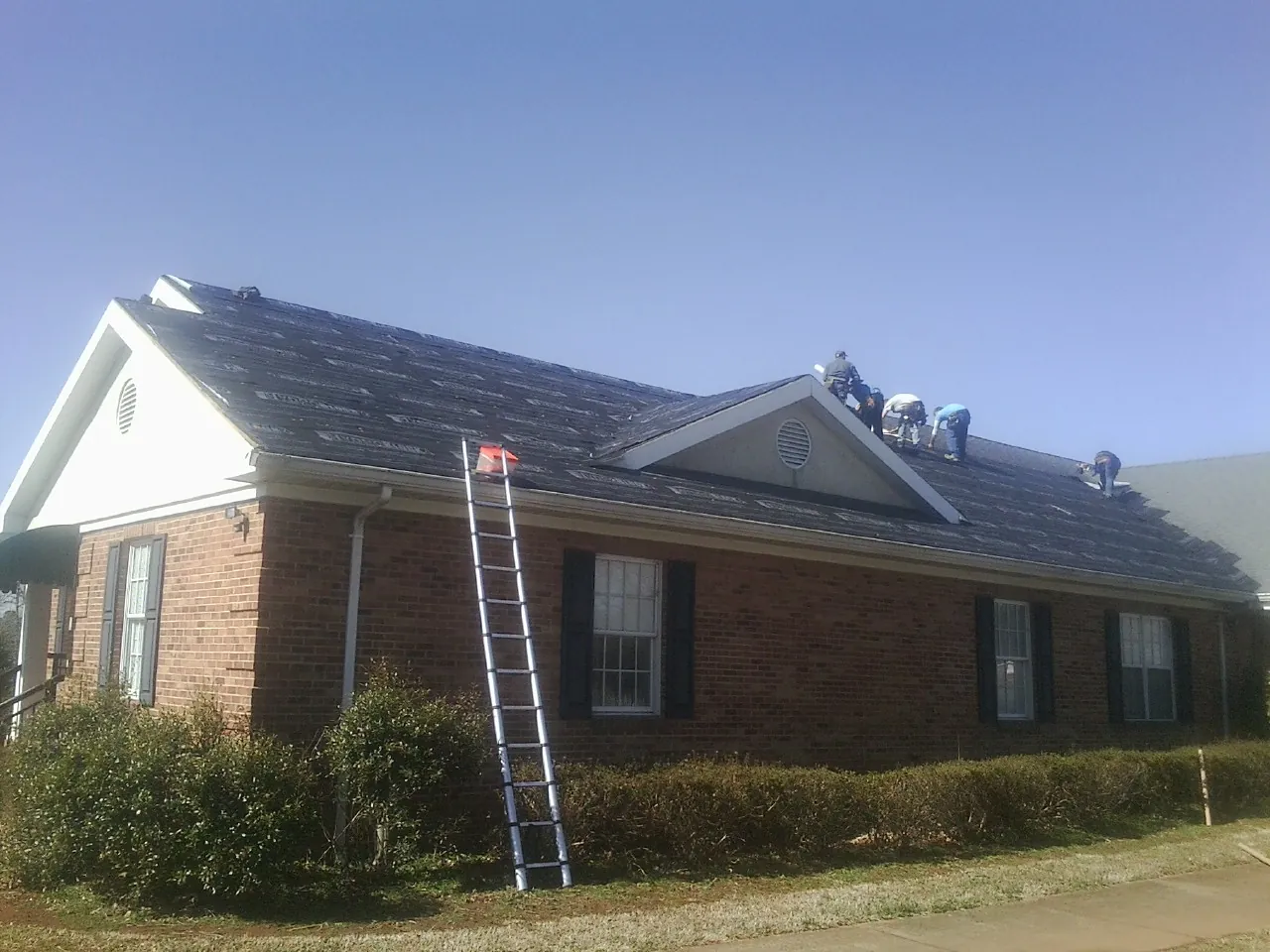 Crew tearing shingles off a brick ranch roof with a ladder set — Emergency Roof Repair work by our crew in Plaistow