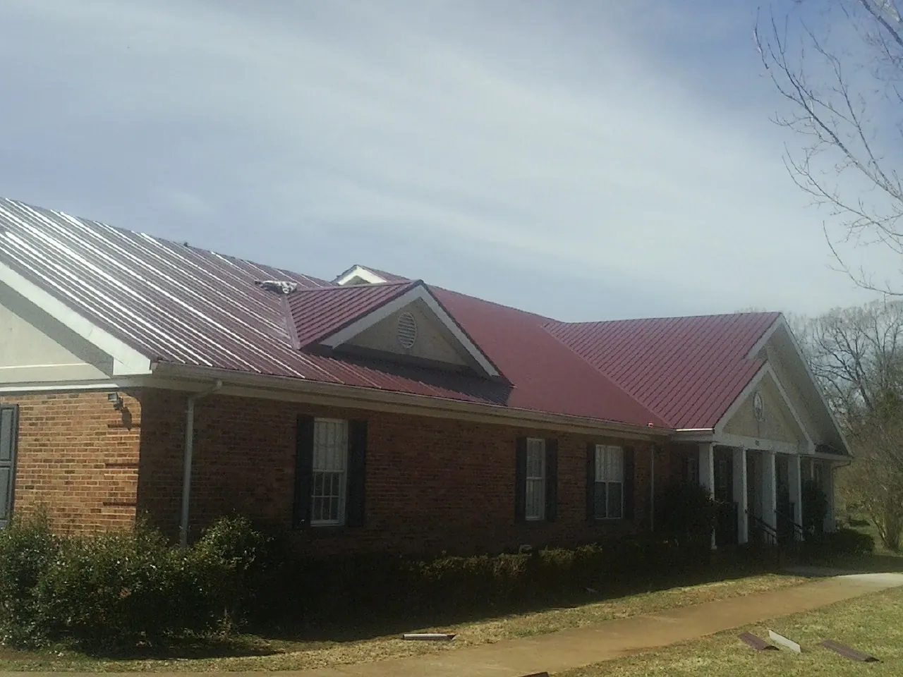 Red metal roof with gabled entries on a long brick building, from a Hail Damage Roof Repair job in Plaistow