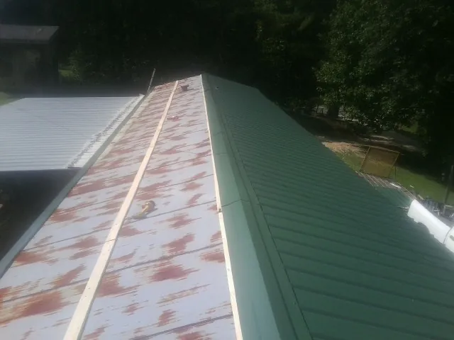 Old rusted panels beside newly installed green metal roofing — Wind Damage Roof Repair by Roofing Brothers in Plaistow