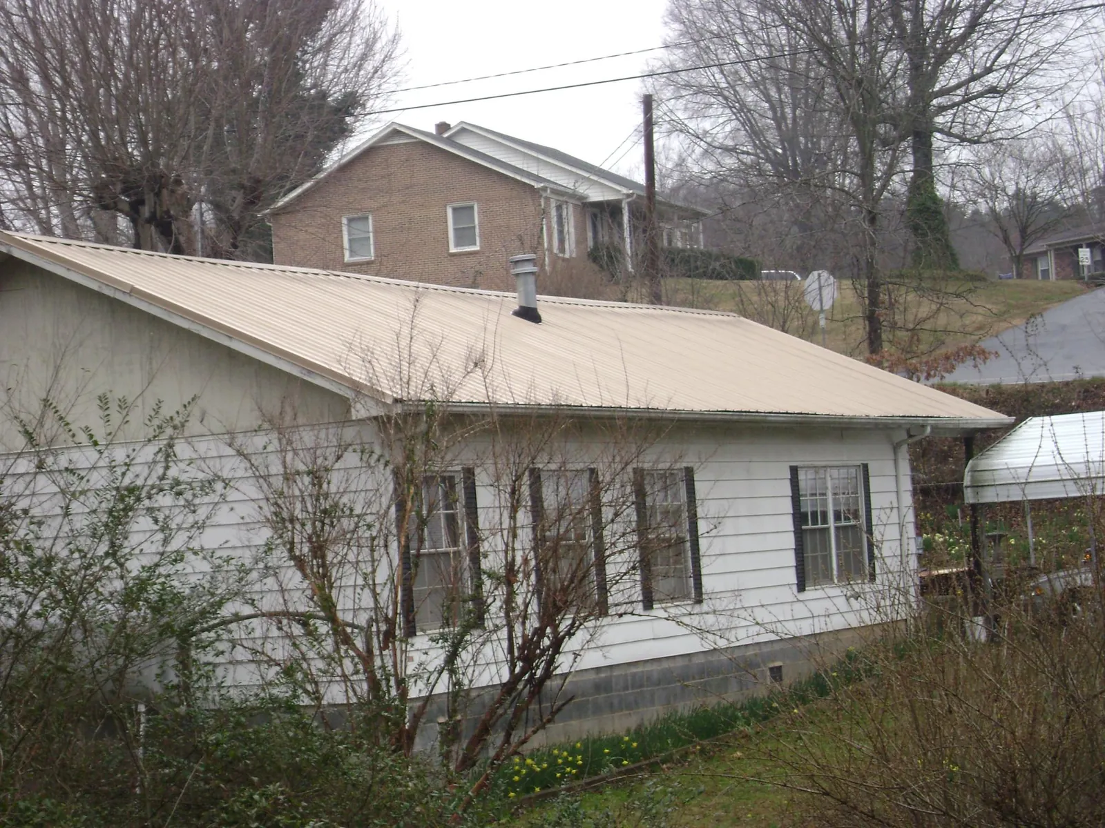 Tan metal roof on a white sided house set into a hillside — Commercial Roofing by Roofing Brothers in Plaistow